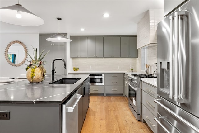 kitchen with a center island with sink, high end appliances, gray cabinets, light wood-style floors, and a sink