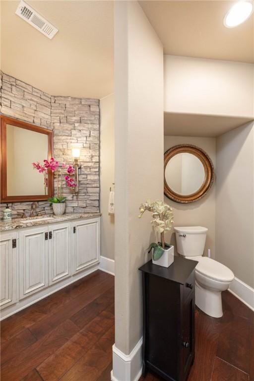 bathroom featuring baseboards, visible vents, toilet, wood finished floors, and vanity