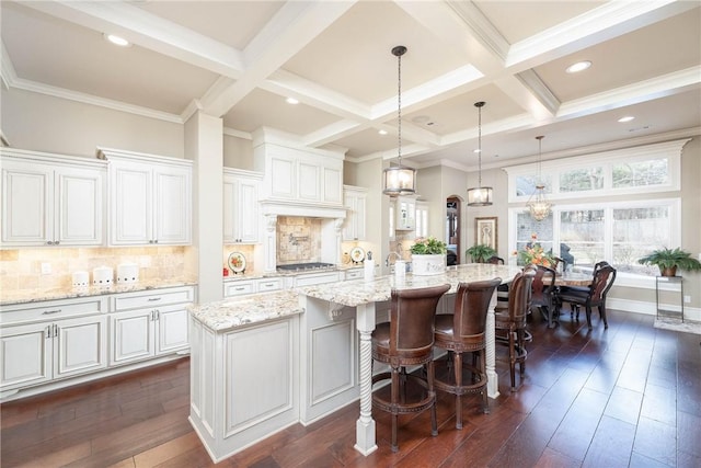 kitchen featuring coffered ceiling, dark wood-type flooring, a kitchen island with sink, stainless steel gas stovetop, and beam ceiling