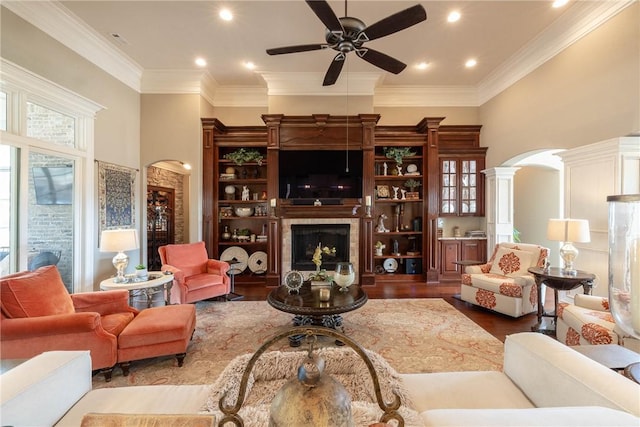 living room featuring arched walkways, a fireplace, ornamental molding, ceiling fan, and wood finished floors