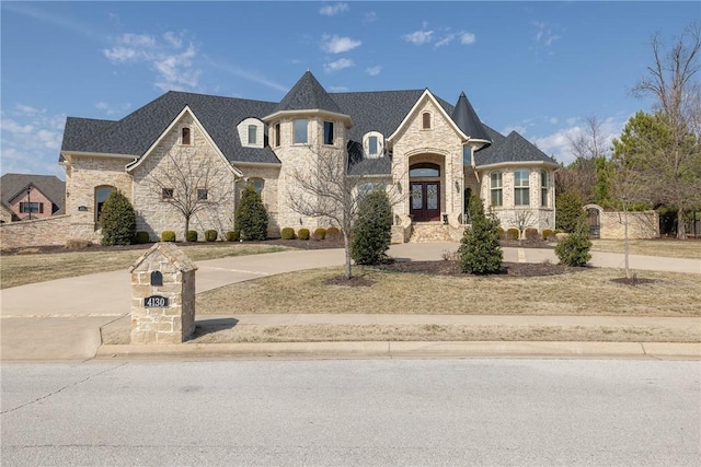 french provincial home with driveway, french doors, stone siding, and fence