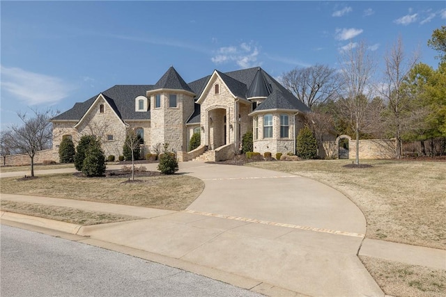 french country inspired facade with driveway, stone siding, and fence