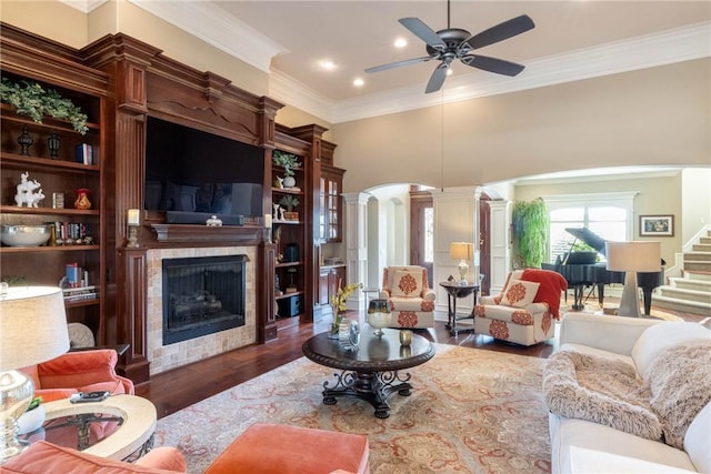 living room featuring arched walkways, a tile fireplace, wood finished floors, stairs, and ornate columns