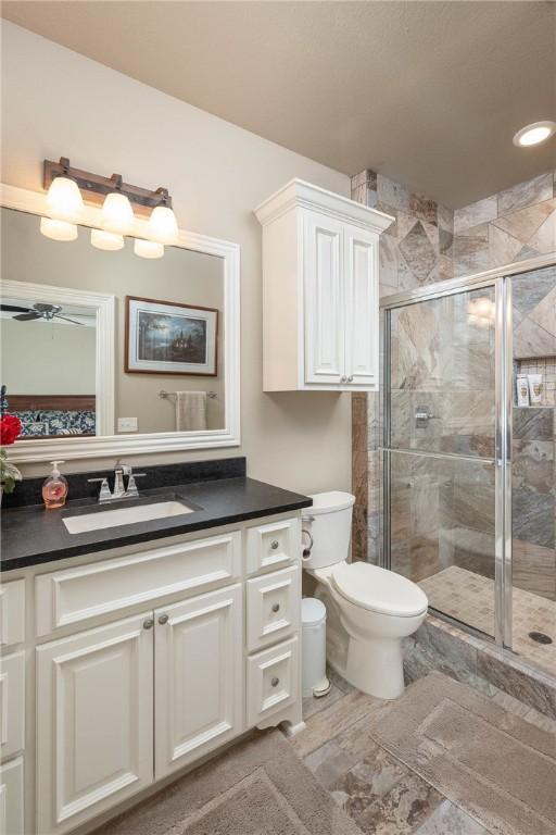 bathroom with toilet, ceiling fan, a stall shower, and vanity