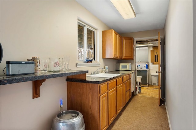 kitchen with white microwave, light colored carpet, a sink, brown cabinets, and dark countertops