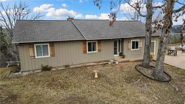 single story home with a patio, a shingled roof, and a chimney