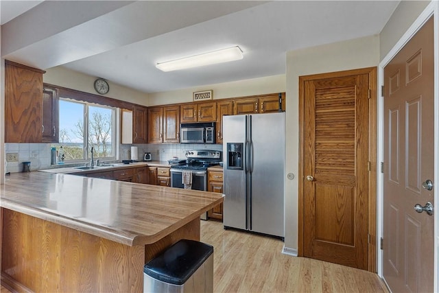 kitchen featuring stainless steel appliances, a peninsula, a sink, and decorative backsplash