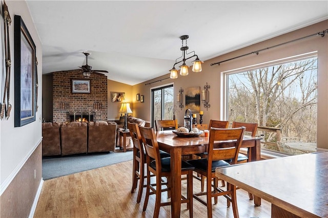 dining area with vaulted ceiling, a brick fireplace, light wood-style flooring, and a ceiling fan