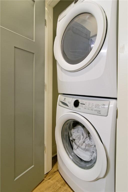 washroom with light wood-type flooring, stacked washing maching and dryer, and laundry area