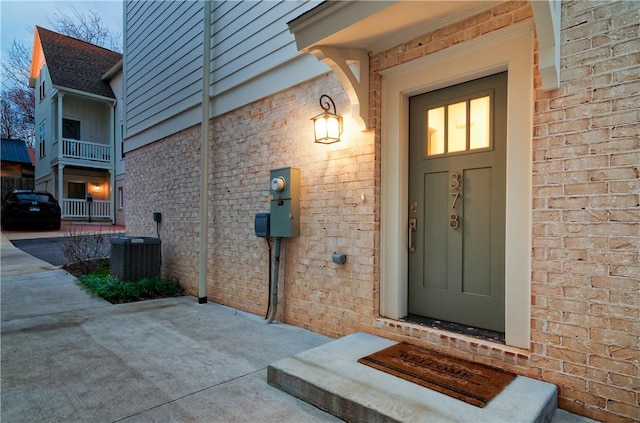 view of exterior entry featuring central AC and brick siding