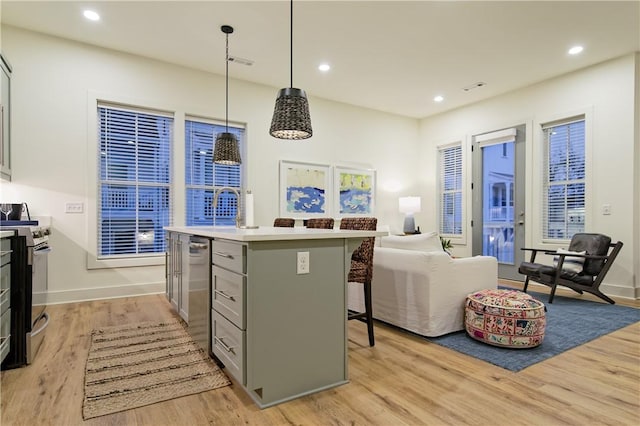 kitchen featuring stainless steel stove, a kitchen breakfast bar, light wood-type flooring, gray cabinets, and a center island with sink