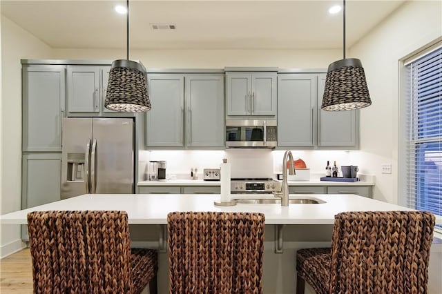 kitchen with a sink, a kitchen breakfast bar, light countertops, appliances with stainless steel finishes, and hanging light fixtures