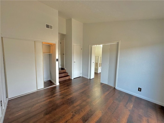 unfurnished bedroom with dark wood-style flooring, a closet, visible vents, high vaulted ceiling, and baseboards