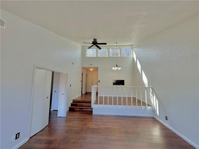 unfurnished living room with stairs, ceiling fan with notable chandelier, wood finished floors, and visible vents