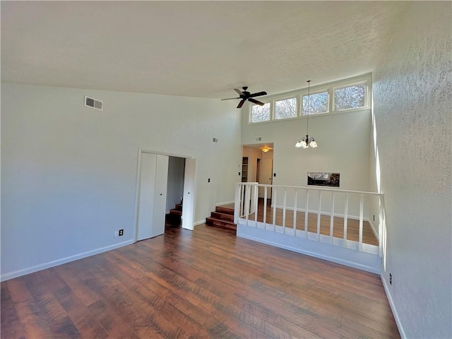 unfurnished room featuring visible vents, stairway, wood finished floors, baseboards, and ceiling fan with notable chandelier