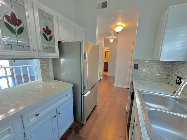 kitchen with a sink, visible vents, white cabinetry, backsplash, and freestanding refrigerator