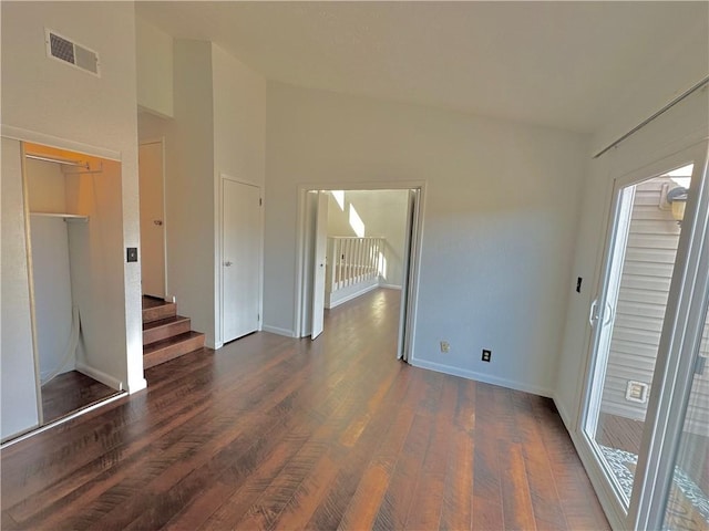 spare room featuring baseboards, visible vents, dark wood finished floors, a high ceiling, and stairs