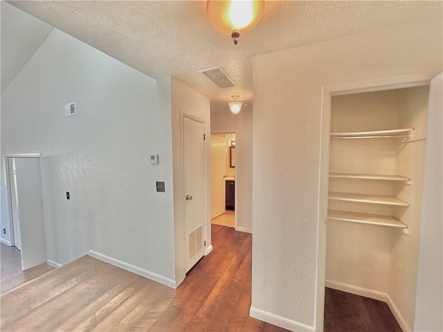 interior space featuring a textured ceiling, a textured wall, wood finished floors, and visible vents