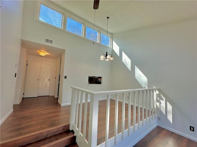 staircase with baseboards, visible vents, wood finished floors, a high ceiling, and a chandelier