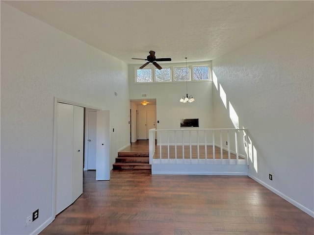 unfurnished living room featuring ceiling fan with notable chandelier, stairway, wood finished floors, and baseboards