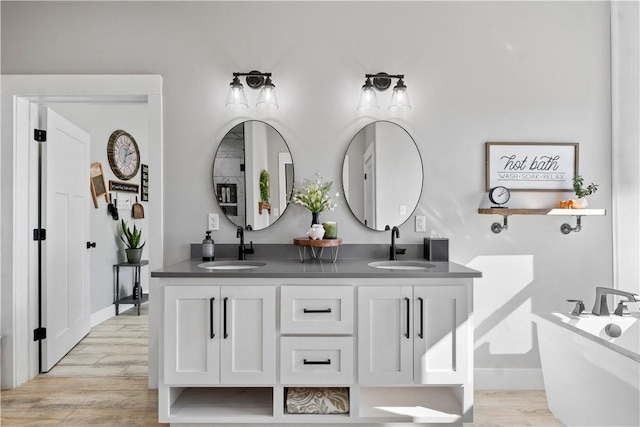 bathroom with double vanity, a freestanding tub, a sink, and wood finished floors