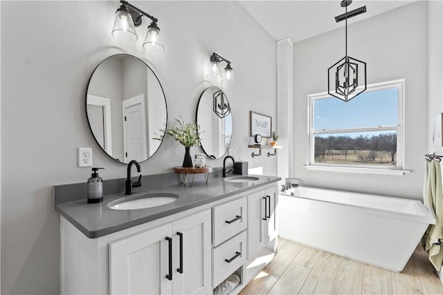 full bath with double vanity, a sink, a freestanding bath, and wood finished floors