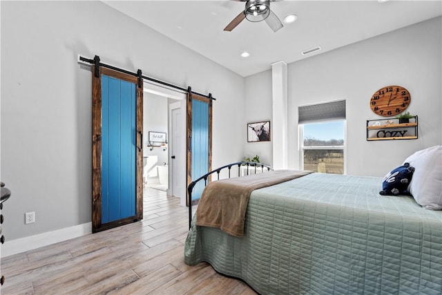 bedroom with a barn door, visible vents, baseboards, a ceiling fan, and light wood-style flooring