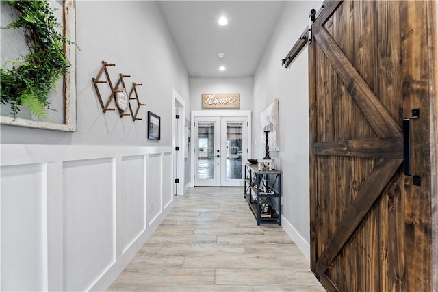 interior space featuring a barn door, light wood-style flooring, recessed lighting, a decorative wall, and french doors