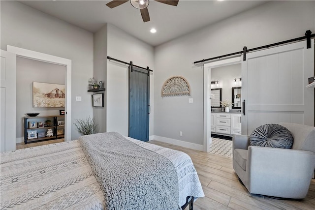 bedroom with light wood finished floors, a barn door, baseboards, ceiling fan, and ensuite bathroom