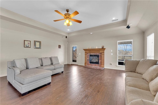 living area featuring dark wood finished floors, visible vents, a brick fireplace, ceiling fan, and baseboards