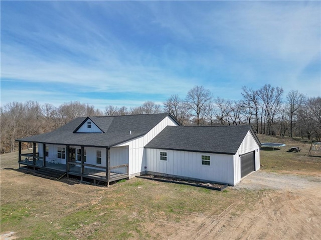 view of front of property with dirt driveway, a front lawn, roof with shingles, and a garage