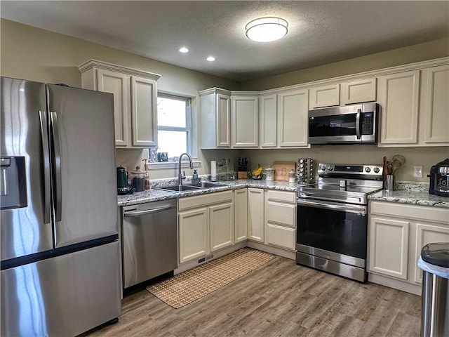 kitchen featuring recessed lighting, light wood-style flooring, appliances with stainless steel finishes, a sink, and light stone countertops