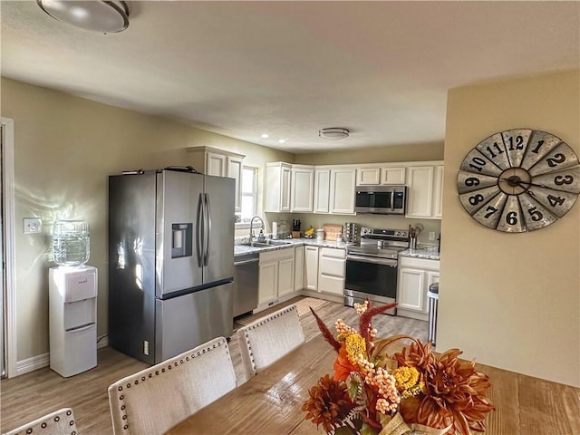 kitchen featuring stainless steel appliances, light wood-style flooring, white cabinetry, a sink, and light stone countertops