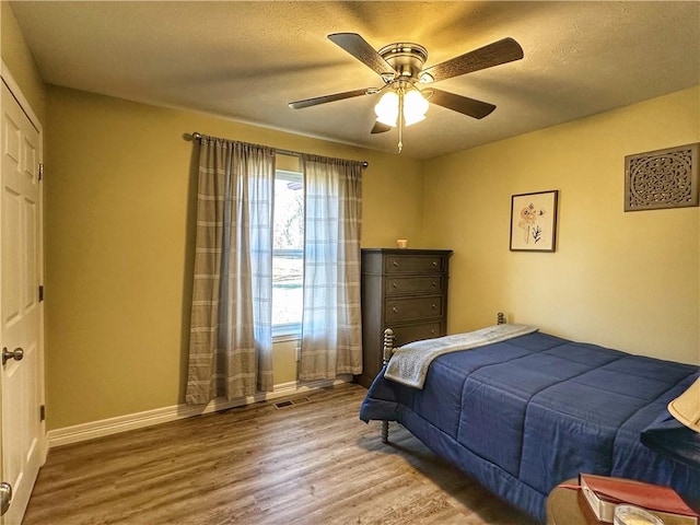 bedroom with a ceiling fan, a textured ceiling, baseboards, and wood finished floors