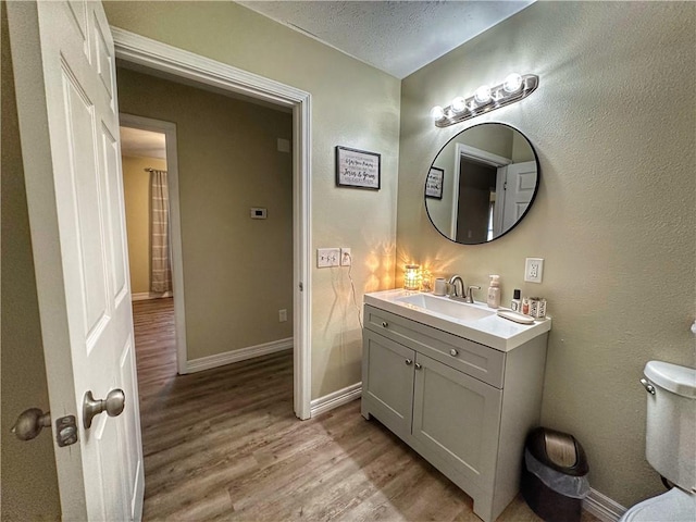 bathroom with a textured ceiling, wood finished floors, vanity, and baseboards