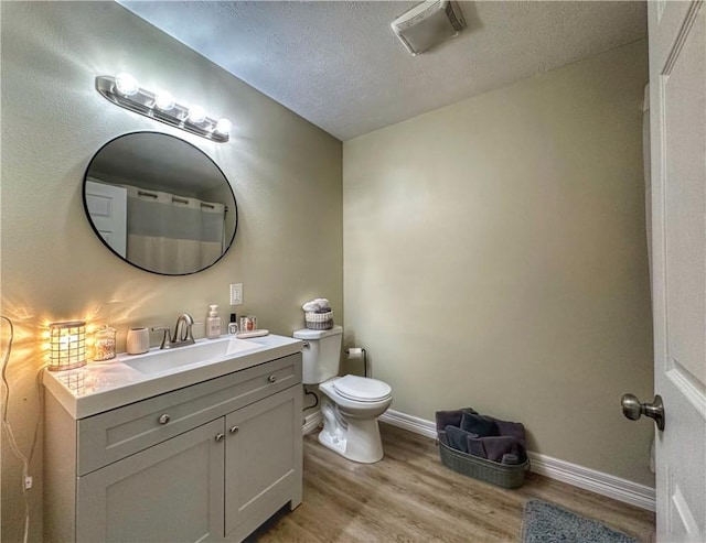 bathroom with visible vents, toilet, vanity, a textured ceiling, and wood finished floors