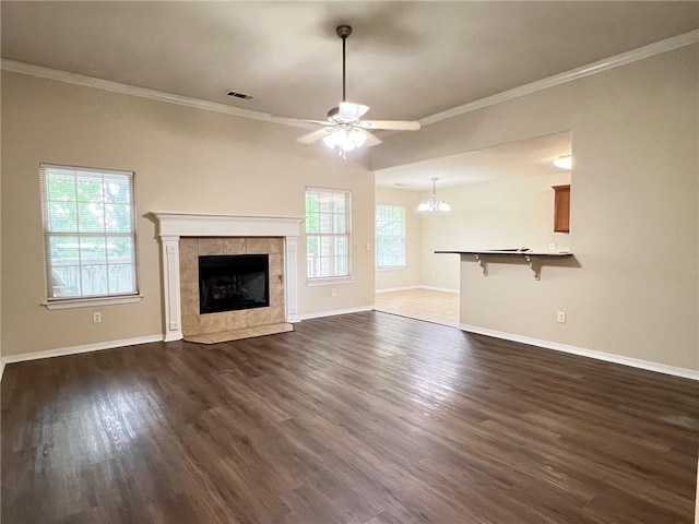 unfurnished living room with ceiling fan with notable chandelier, baseboards, ornamental molding, a tiled fireplace, and dark wood finished floors