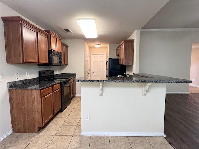 kitchen with visible vents, dark stone counters, a breakfast bar area, a peninsula, and black appliances