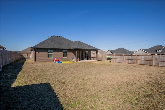 rear view of house with a shingled roof, a lawn, a patio area, and a fenced backyard