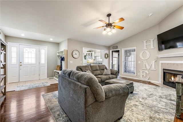 living area featuring ceiling fan, hardwood / wood-style flooring, a fireplace, baseboards, and vaulted ceiling