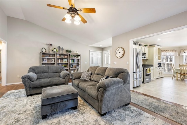 living area with light wood-type flooring, lofted ceiling, baseboards, and a ceiling fan