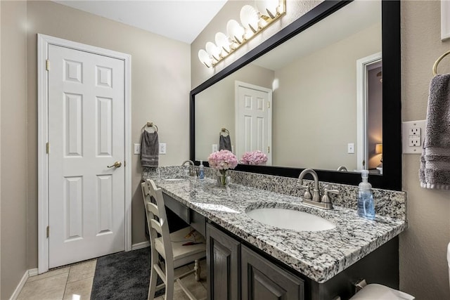 bathroom featuring baseboards, double vanity, a sink, and tile patterned floors