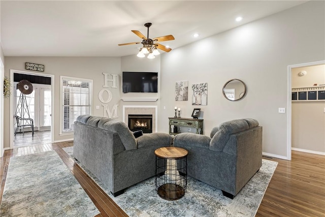 living area featuring baseboards, lofted ceiling, wood finished floors, a lit fireplace, and recessed lighting