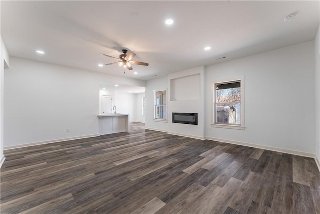 unfurnished living room with a glass covered fireplace, ceiling fan, dark wood-style flooring, a sink, and recessed lighting