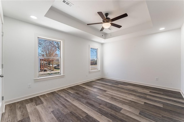 spare room with a tray ceiling, dark wood-type flooring, visible vents, and baseboards