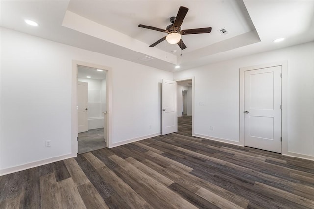 unfurnished bedroom featuring dark wood-type flooring, a raised ceiling, baseboards, and ensuite bathroom