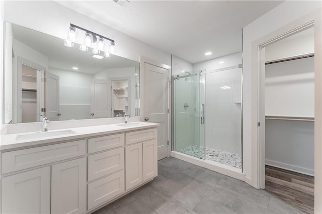 full bath with double vanity, a shower stall, a walk in closet, and a sink