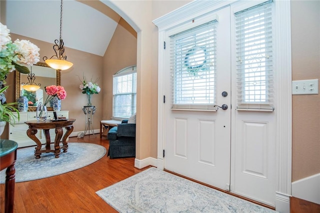 foyer with arched walkways, baseboards, wood finished floors, and lofted ceiling