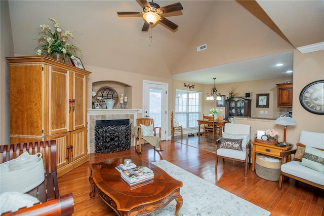 living room featuring light wood-type flooring, a fireplace, visible vents, and ceiling fan with notable chandelier