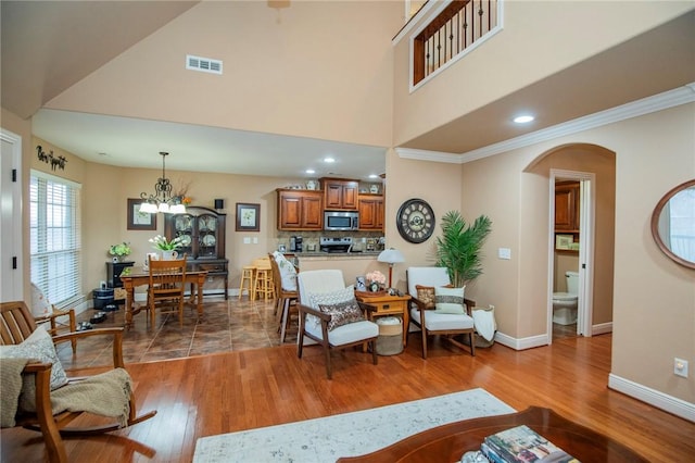 living room with baseboards, visible vents, arched walkways, an inviting chandelier, and light wood-style floors